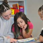 Sequim Gazette photo by Matthew Nash/ Maddy Schroeder, an eighth grader, reads Cat Kid Comic Club with second graders Eliza Burns and Kamaria Stipe at Greywolf Elementary.