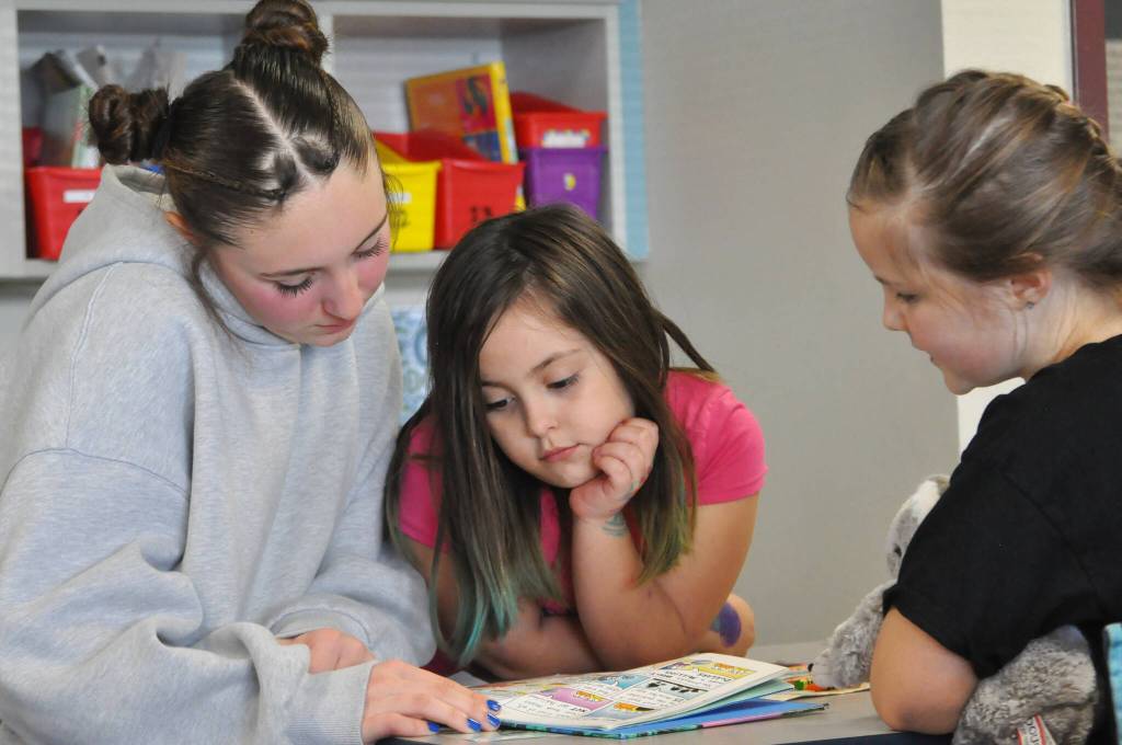 Sequim Gazette photo by Matthew Nash/ Maddy Schroeder, an eighth grader, reads Cat Kid Comic Club with second graders Eliza Burns and Kamaria Stipe at Greywolf Elementary.