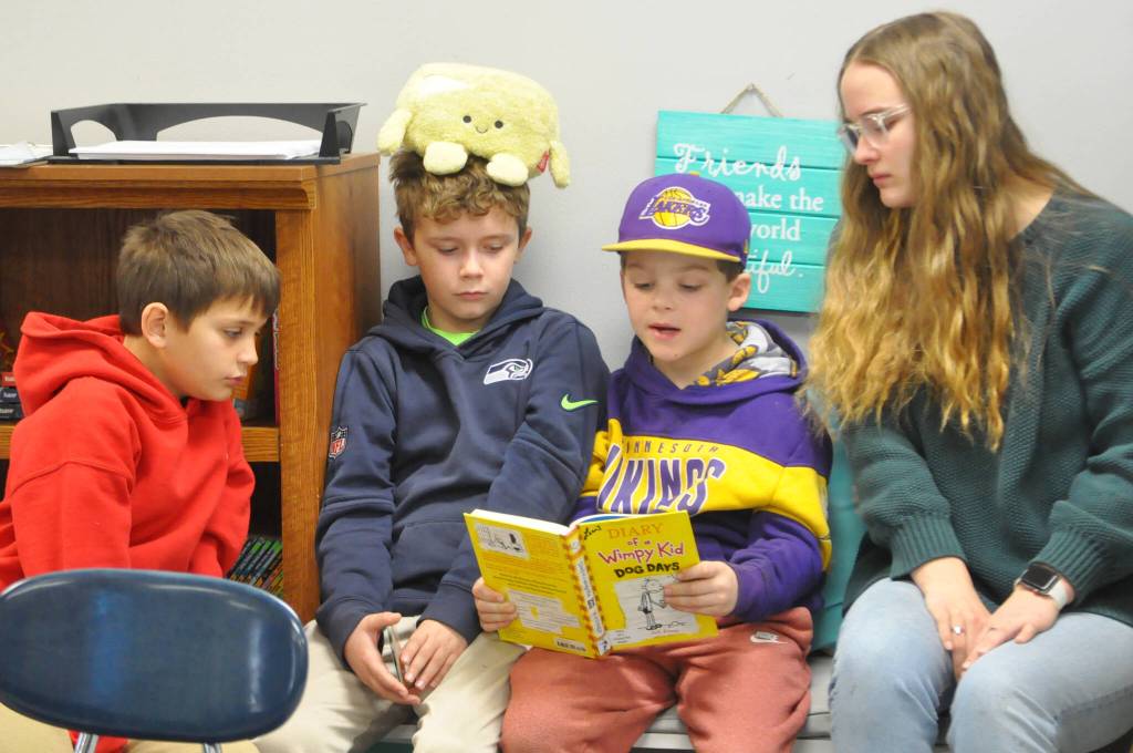 Sequim Gazette photo by Matthew Nash/ Third grader Logan Horn, third from left, reads Diary of a Wimpy Kid: Dog Days to classmates Grayson Rocha and Weston Fuller and sophomore Sariah Weller for Sequims tradition of Read Across America Day.
