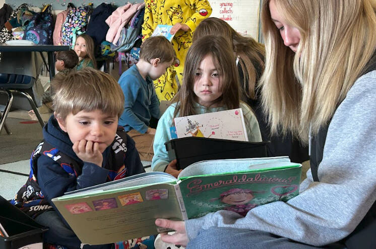 Sequim Gazette photo by Matthew Nash/ Eighth grader Alexia Fuller, on right, reads Emeraldalicious to Greywolf kindergarteners Micah Brooks and Faye Hilliard on March 7.