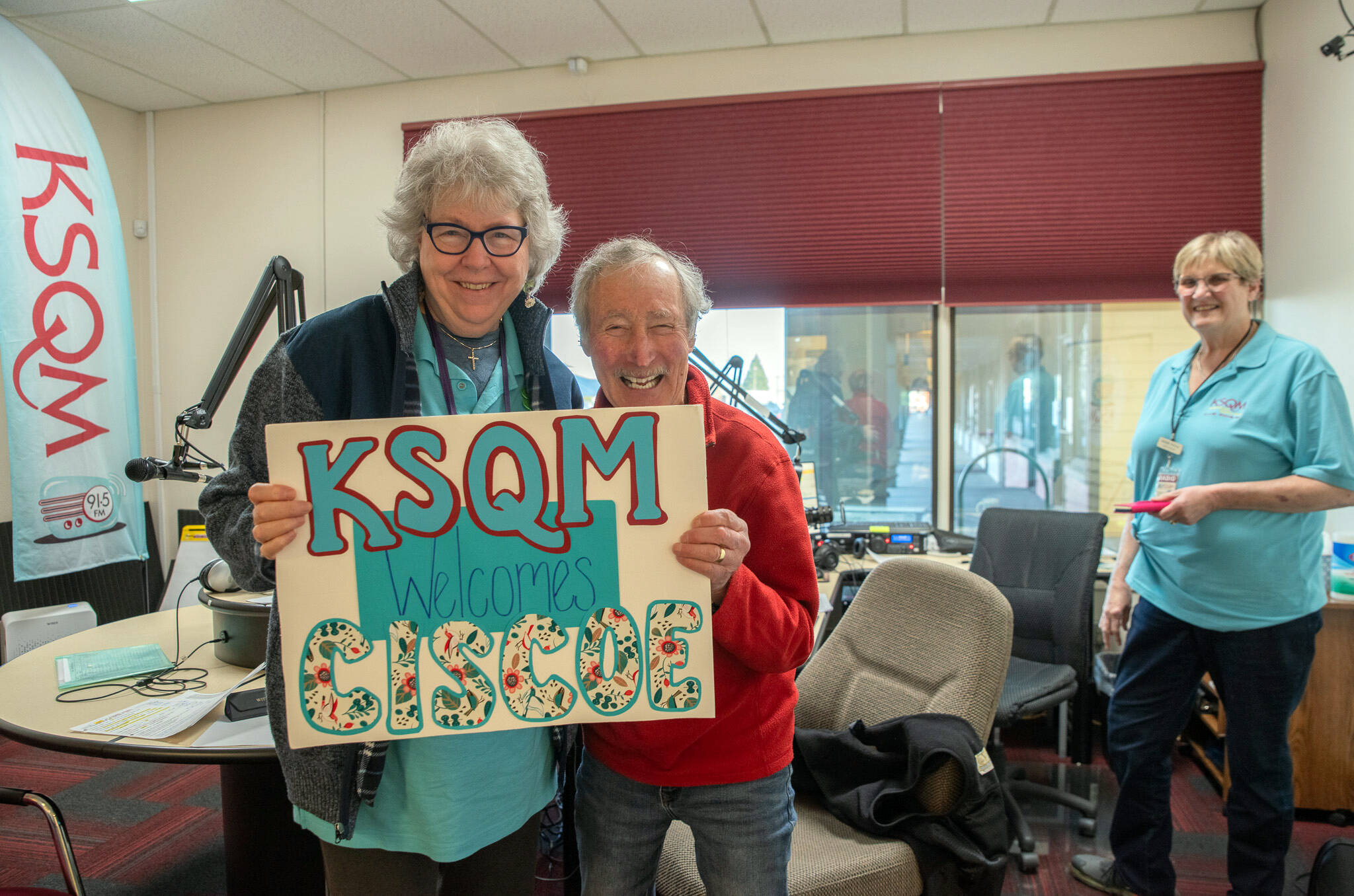 Sequim Gazette photo by Emily Matthiessen
 On March 1, Ciscoe Morris visits the KSQM headquarters and is presented with a welcoming poster by Tama Bankston, administrative director, while his broadcasting partner, Sassy Susan Sorensen looks on.
