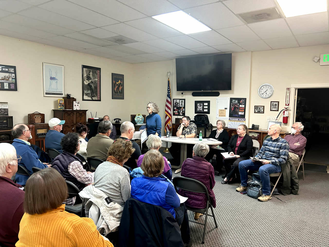 Photo by Kathy Cruz| Susan Fisch (standing), chair of the Clallam County Charter Review Commission, addresses a crowd of Local residents who packed the meeting room at KSQM FM (91.5) last Wednesday evening for the first of several town hall events. Speakers were allowed up to three minutes to share their views about issues related to the charter that they consider most important.