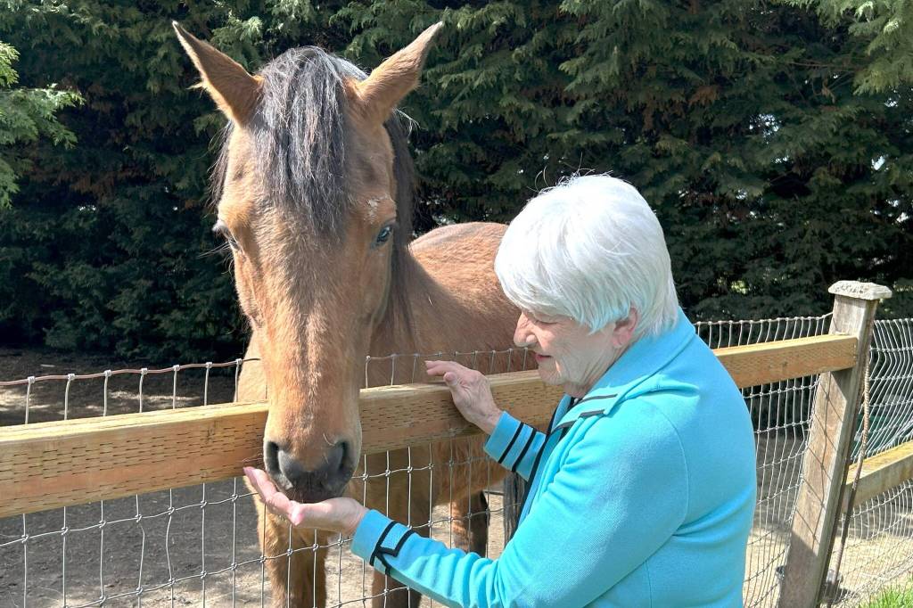 Sequim Gazette photo by Matthew Nash/ Judy Larimore greets her horse Sierra on a sunny Sequim day last week. Larimore moved to Sequim in the early 2000s and planted 200-plus trees and bushes to create a haven for she and her animals.