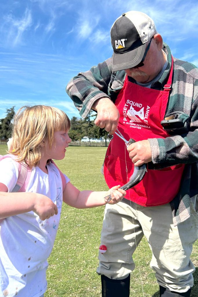 At left, Riley Lemon holds her fish while Chris Coventon with the North Olympic Peninsula Chapter of Puget Sound Anglers takes the hook out. She caught the fish during a field trip to the City of Sequims Water Reuse Demonstration pond in Carrie Blake Community Park.