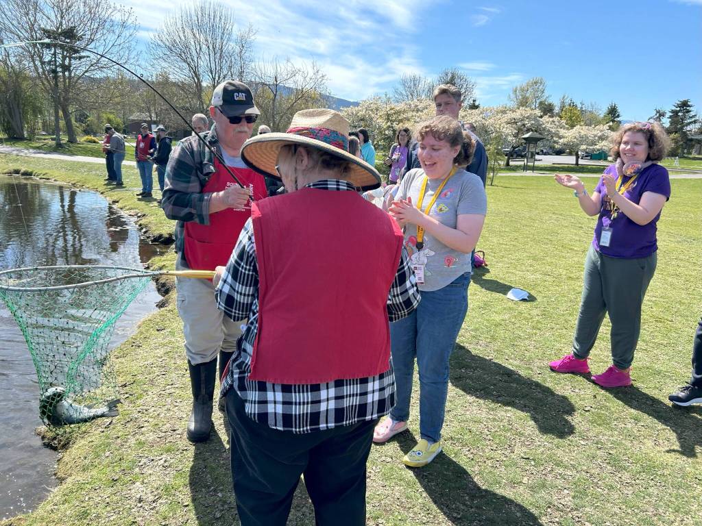 Sequim Gazette photo by Matthew Nash/ Megan Damon, third from left, with twin sister Madison, on right, celebrate her catching a fish on April 18. She and North Olympic Peninsula Chapter of Puget Sound Anglers volunteers reeled in a fish that Madison originally caught but it pulled her fishing pole out of her hands and into the water. Volunteers saw the bobber circling the pond and they and Madison reeled it in.