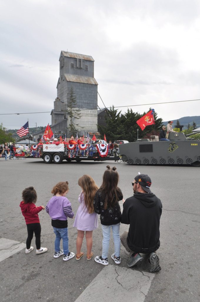 Sequim Gazette photo by Matthew Nash/ Cody Hanning, on right, watches the Grand Parade with his daughters, niece and family-friend as the Mt. Olympus Detachment of the Marine Corps League drives in front of the Sequim grain elevator.