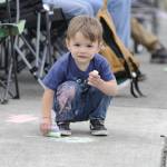 Sequim Gazette photo by Matthew Nash/ Two-year-old Jackson Guyver of Port Angeles passes time waiting for the Grand Parade to start drawing with chalk along Washington Street with his family.