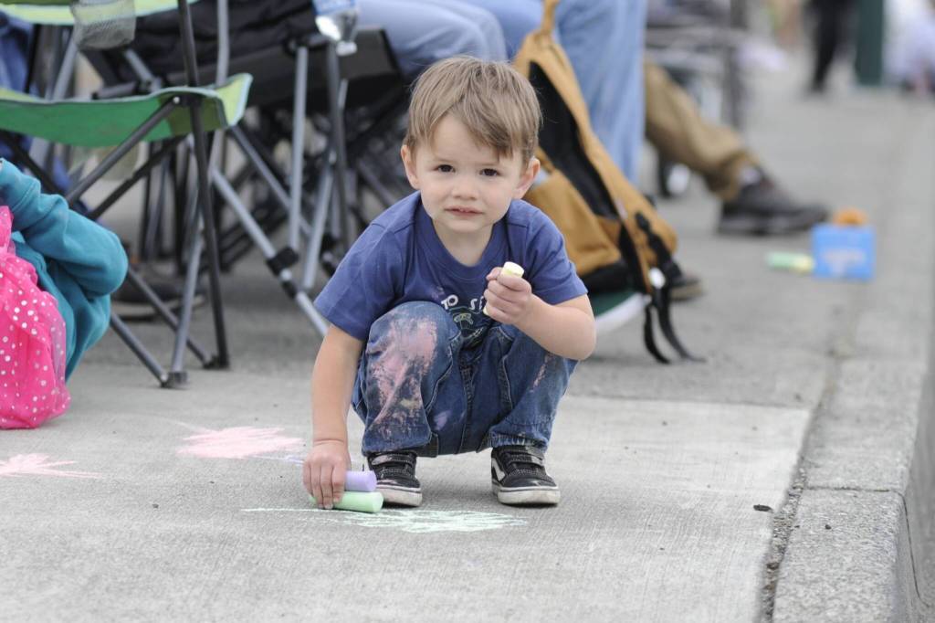 Sequim Gazette photo by Matthew Nash/ Two-year-old Jackson Guyver of Port Angeles passes time waiting for the Grand Parade to start drawing with chalk along Washington Street with his family.