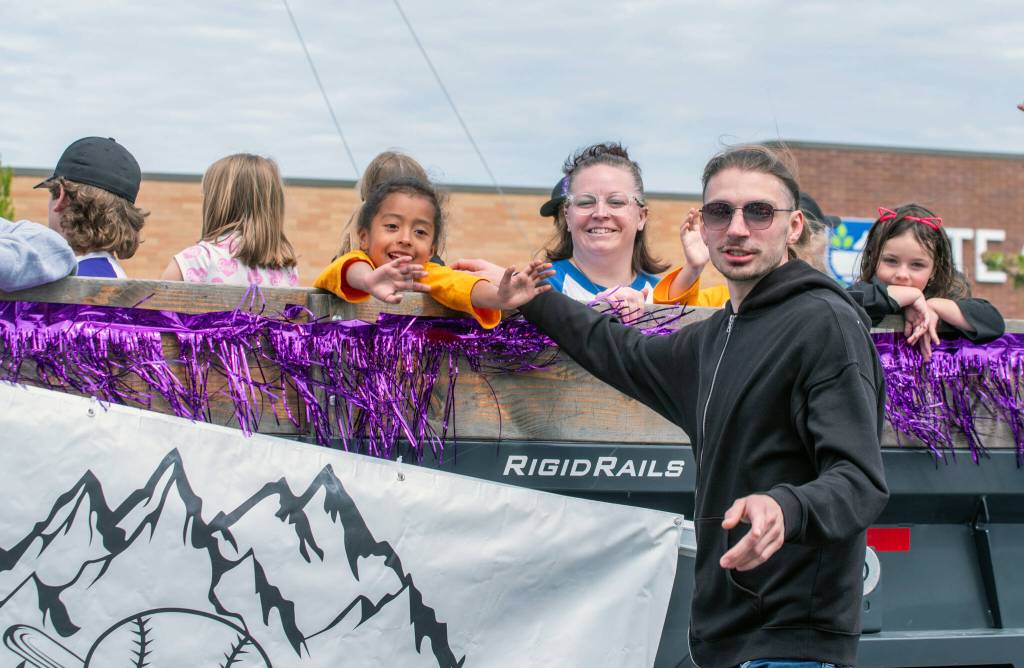 Sequim Gazette photo by Emily Matthiessen/ Anais, age 6, greets her father Oliver as she rides with the Little League of Sequim and the two of them direct their attention to other members of the family.