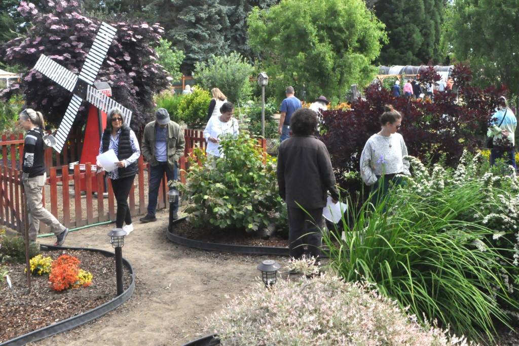 Participants in the Petals Pathways Home Garden Tour traverse through the Harvest Haven/JR Farmstand on June 28.