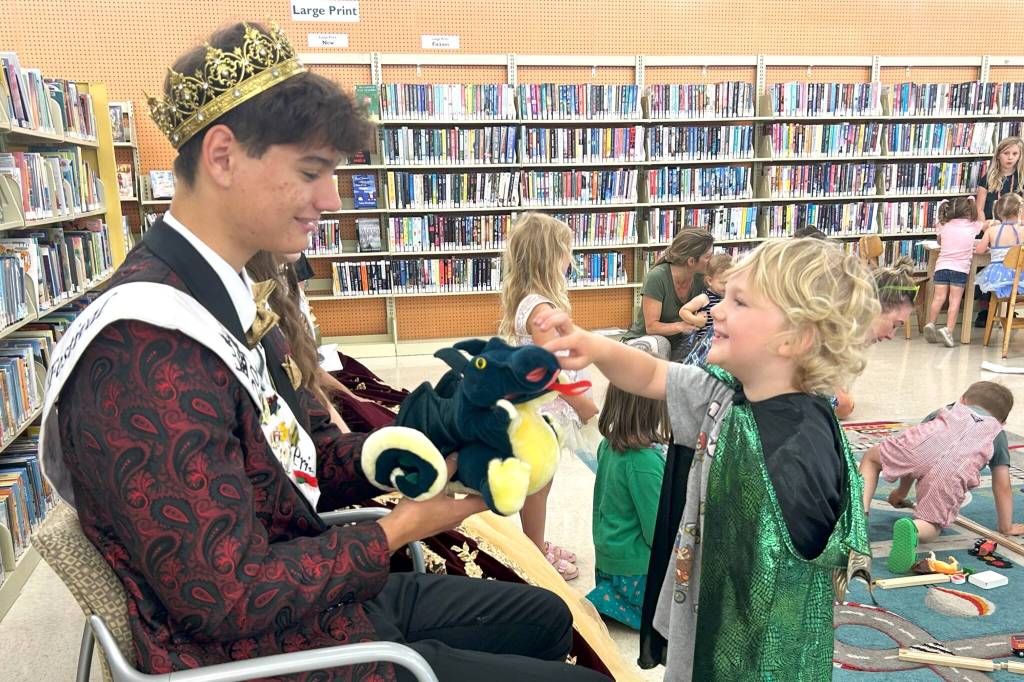 Sequim Gazette photo by Matthew Nash/ James Lynn, 3, dressed as a dragon, talks with Sequim Irrigation Festival Prince Malachi Byrne about dragons after Storytime with the Royal Court. James father Pat said it was his familys first time at Storytime with the North Olympic Library System and hes known Malachi since he was a little boy.