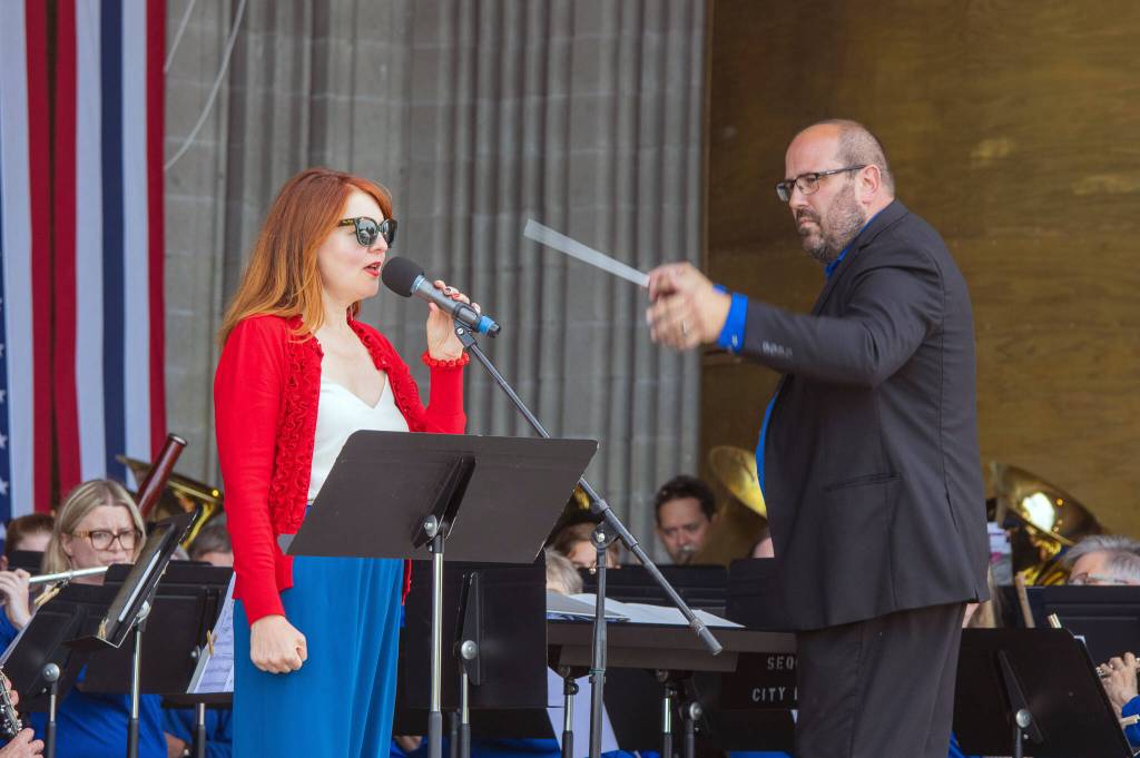 Sequim Gazette photo by Emily Matthiessen/ Sarah Shea sings with the Sequim City Band while Tyler Benedict conducts during the Independence Day celebration at Carrie Blake Community Park.