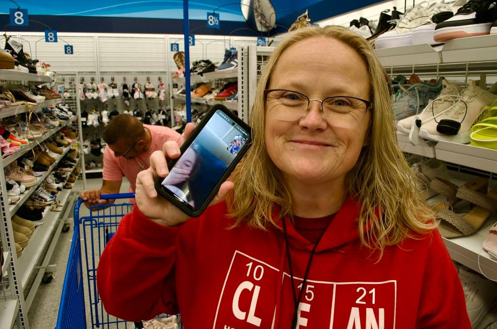 Sequim Gazette photo by Jacques Star/ Tammy Blessing holds up her cell phone, through which she is communicating with her daughter, Taylor White. She and her husband Cassidy Blessing (behind her) shop for a new pair of school shoes for Taylor with a gift card provided by H.U.M.A.N., a new Sequim nonprofit created by Cassidys former bosses, Darrin and Alicia Liggins.
