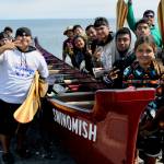Sequim Gazette photo by Jacques Star/ Chas James, left, holding paddles, and Danielle James (right, in traditional dress), along with their Swinomish Tribe canoe mates, gather their paddles after reaching the shore at Jamestown Beach, where they were greeted by members of the Jamestown SKlallam Tribe and others after completing another leg of the annual Canoe Journey. The Paddle to Elwha was hosted by the Lower Elwha Klallam Tribe. The protocol and celebration took place Aug. 1-5.