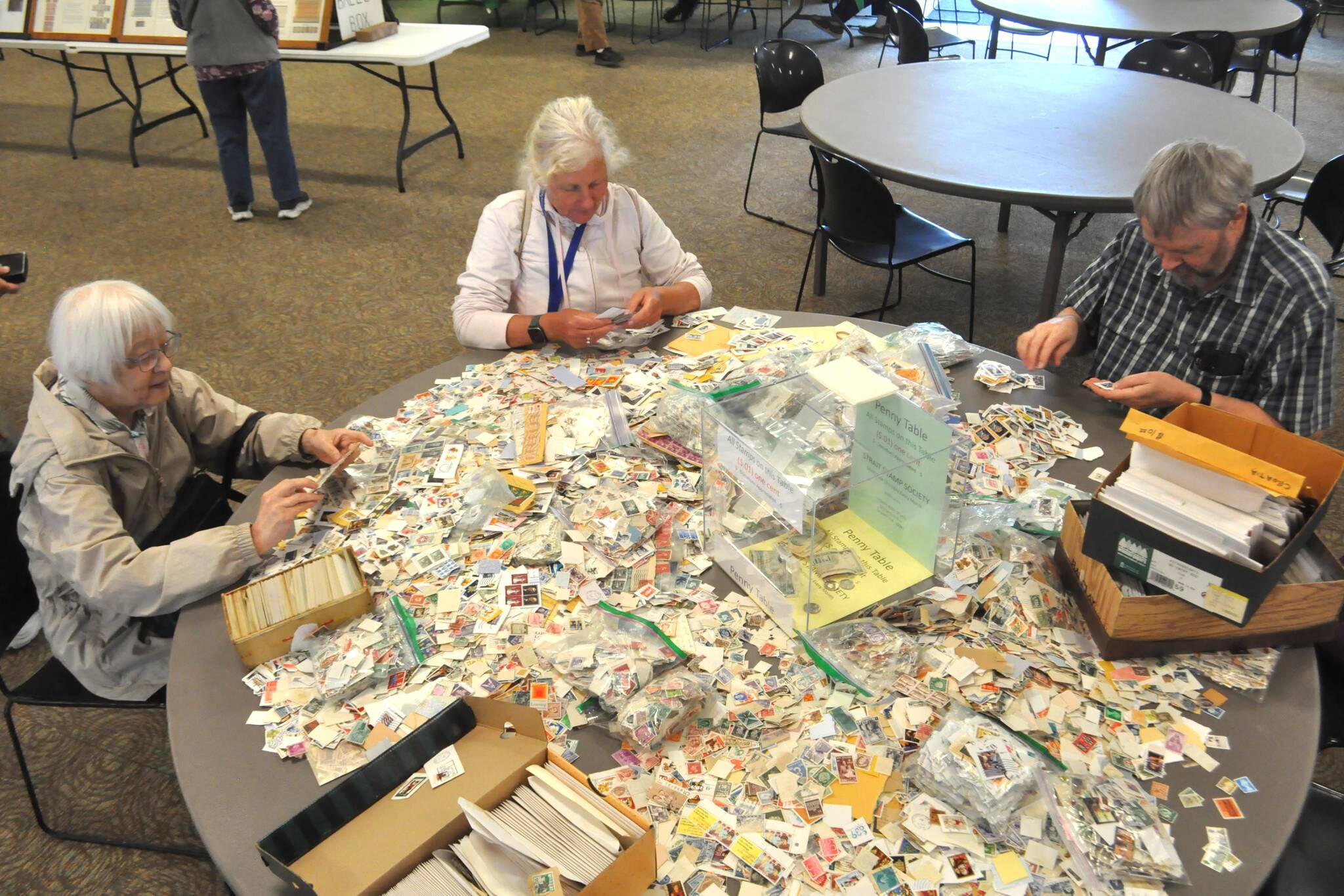 Sequim Gazette photos by Matthew Nash
Members of the Victoria Stamp Club, from left, Esther Monasch, Cheryl Thomas and Ken P. (who preferred not to give his last name) search through the Penny Table at the Strait Stamp Show on Aug. 9 in the Guy Cole Event Center. Monasch, who has come to the show for 10 years, said the most interesting part is the thrill of hunting.