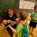 Carol Koenig (left) with Sequim Community Youth Orchestra shows Lucas Wright what its like to play a note on a violin as Caleb Wright (right) looks on.