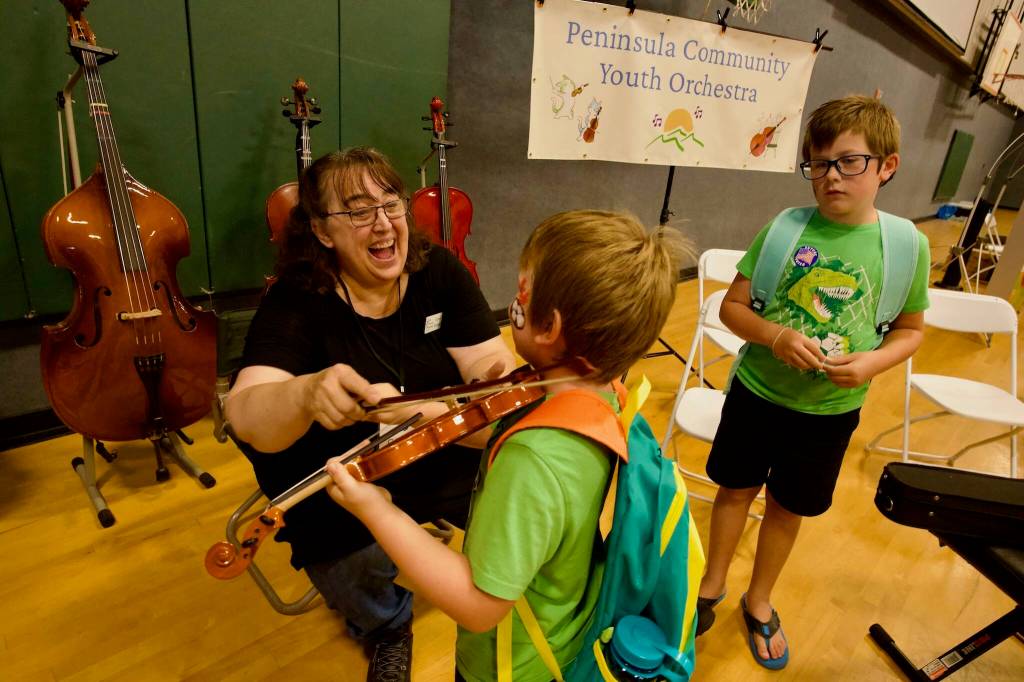 Carol Koenig (left) with Sequim Community Youth Orchestra shows Lucas Wright what its like to play a note on a violin as Caleb Wright (right) looks on.