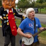 Steve Koehler of Sequim plays his banjo and sings This Land is Your Land with a caricature of Trump walking behind him.