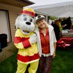 Event organizer Becky Penrose poses with Clallam County Fire District 3's  Sparky the Fire Dog as attendees of Saturday's community picnic enjoy burgers from Sequim's Black Bear Diner.