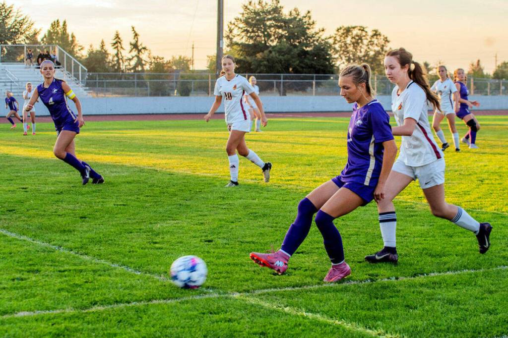 Photo by Emily Matthiessen for Olympic Peninsula News Group/ Sequims Kiley Winter sends a pass upfield as teammate Raimey Brewer, far left, looks on during the Wolves season-opener against Kingston on Sept. 11. Winter scored a goal for Sequim, but the Buccaneers came out on top 2-1 in the Olympic League contest.