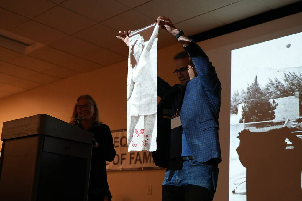 Photo by Michael Dashiell/ JD Angiuli, master of ceremonies for the Sequim High School Hall of Fame, holds up a towel with a photo of Branette (Smith) Richards, a 2025 inductee, projected onto it.
