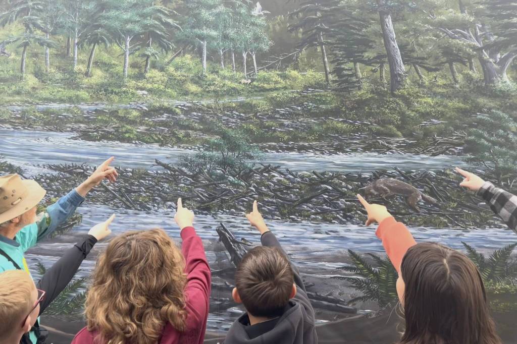Sequim Gazette photo by Matthew Nash/ Students do a search for various animals, including an elk, on a Tim Quinn mural on the side of the Dungeness River Nature Center with help from Olympic Peninsula Audubon Society volunteer Bob Boekelheide.