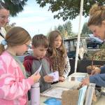 Sequim Gazette photo by Matthew Nash/ Parent-volunteer Sam Touchie, on left, with Helen Haller Elementary students Sadie Touchie, Lucas Stout, and Peyton Winter greet Sarah Bones, director of Five Acre School, at the schools booth during the Dungeness River Festival to learn about composting, the watershed, and more.