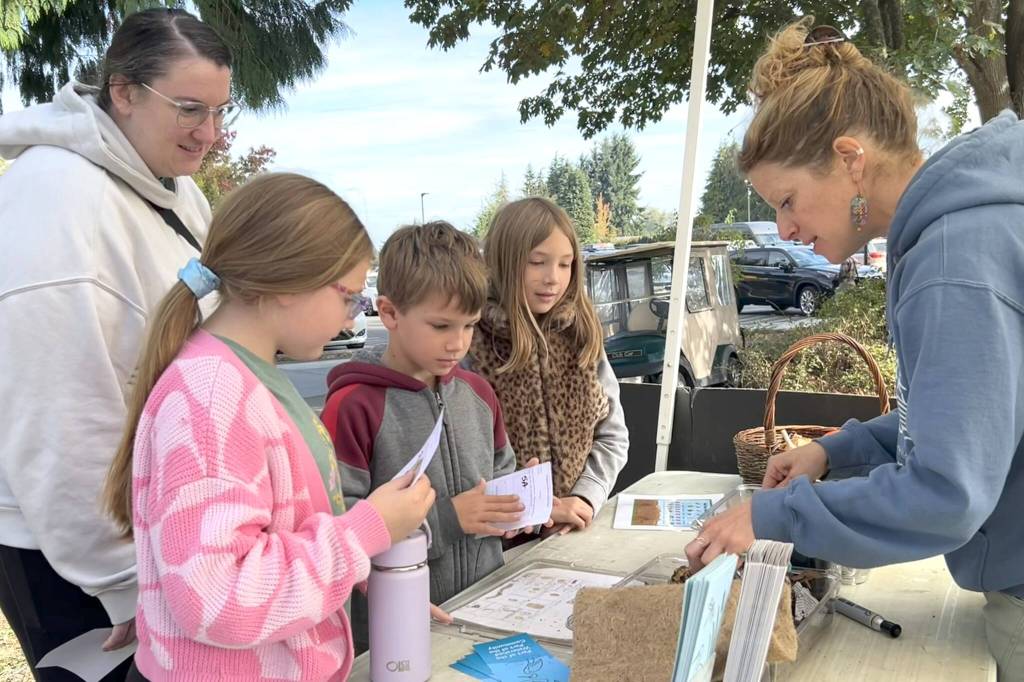 Sequim Gazette photo by Matthew Nash/ Parent-volunteer Sam Touchie, on left, with Helen Haller Elementary students Sadie Touchie, Lucas Stout, and Peyton Winter greet Sarah Bones, director of Five Acre School, at the schools booth during the Dungeness River Festival to learn about composting, the watershed, and more.