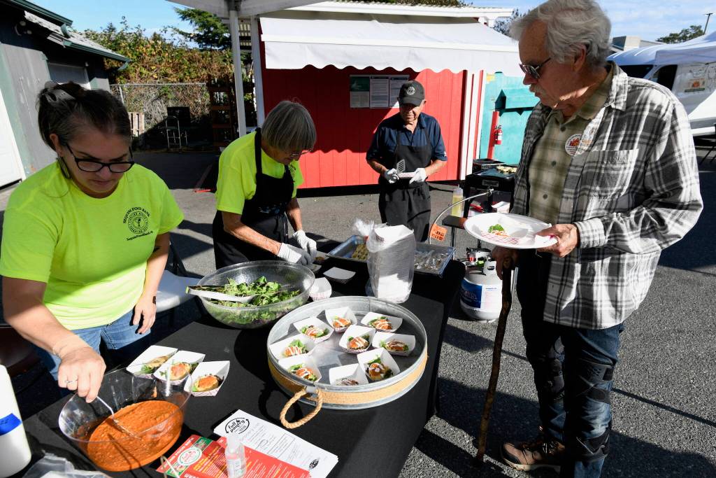 Sequim Gazette photo by Jacques Star/
John Flower stops by a booth at Sequim Food Banks Everyone at the Table fundraiser where Nicole Hartman of Sequim Sunrise Rotary prepares Romesco sauce to serve with crabless cakes.