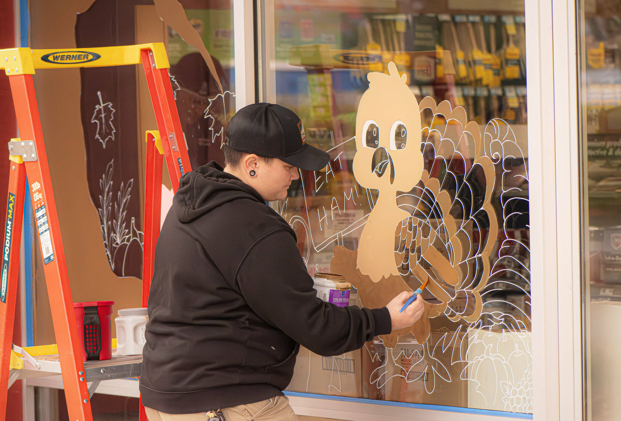 Sequim Gazette photo by Monica Berkseth/ In a nod to the upcoming Thanksgiving holiday, Sherwin-Williams Paint Store employee - and artist - Halie Williams paints a humorous EAT HAM! message alongside a turkey on the front window of the store located at 1400 W. Washington St. Williams decorated the window for Halloween and said she intends to paint it for all major holidays going forward.