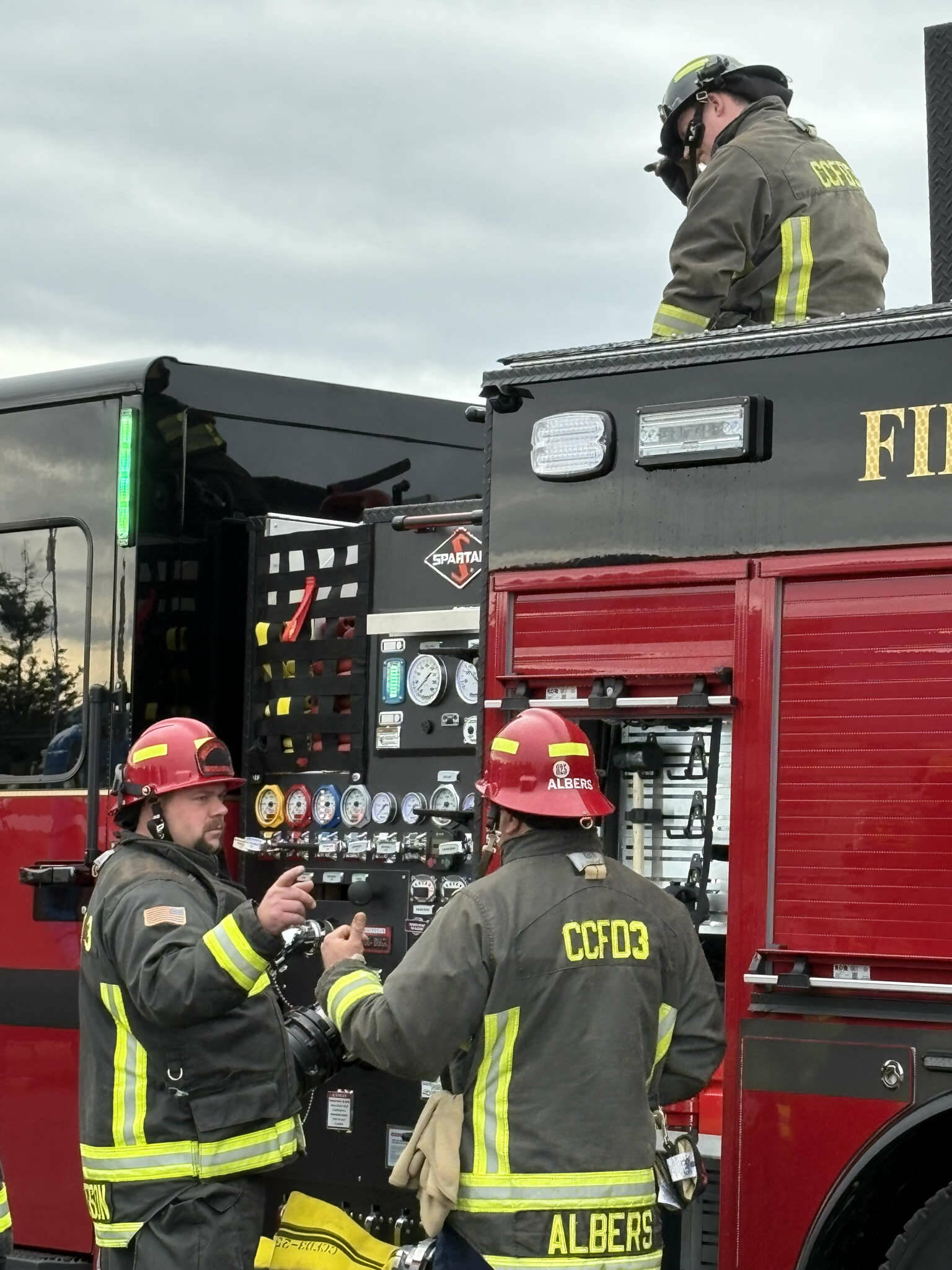 Photo courtesy CCFD3/ Captains Jeff Albers and Travis Anderson with Clallam County Fire District 3 discuss training on a new fire engine while Firefighter Ryan Hueter loads the hose.
