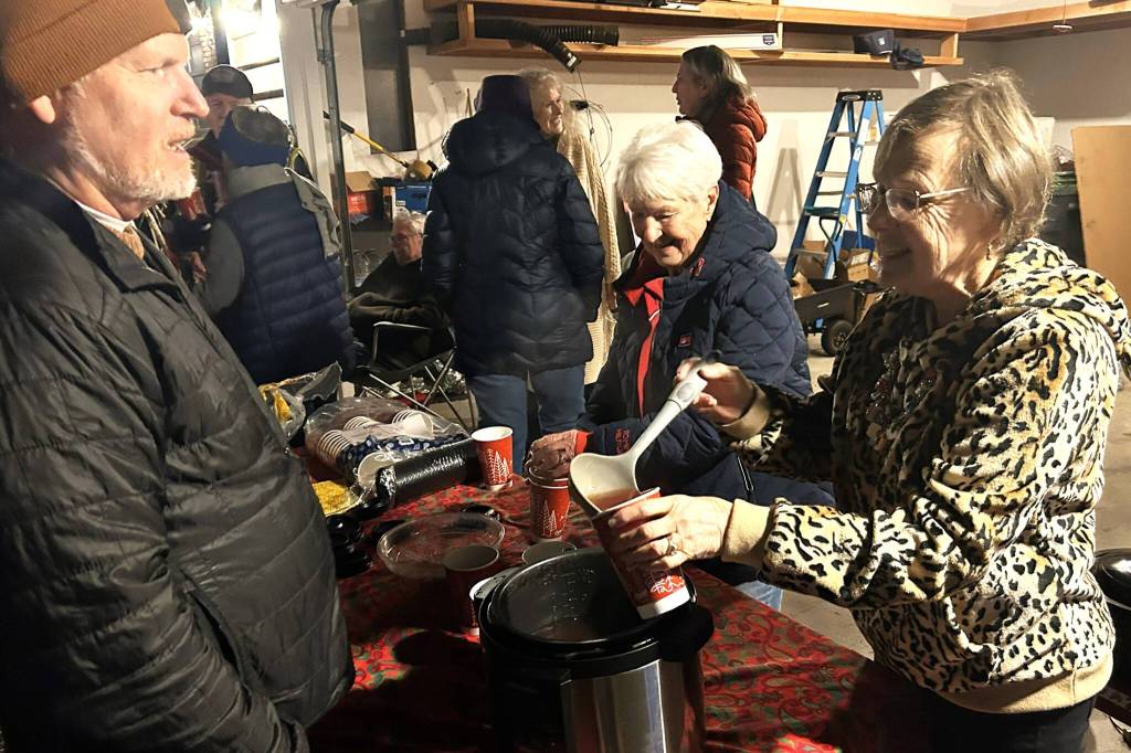 Sequim Gazette photo by Matthew Nash
Karen Eldridge, on right, pours a warm apple cinnamon drink for Brian Hanley as Barb Parse prepares another drink during a Sunland block party on Dec. 11. Neighbors offer cookies, warm drinks and a campfire each year as they await Santas Toy and Food Fire Brigade.
