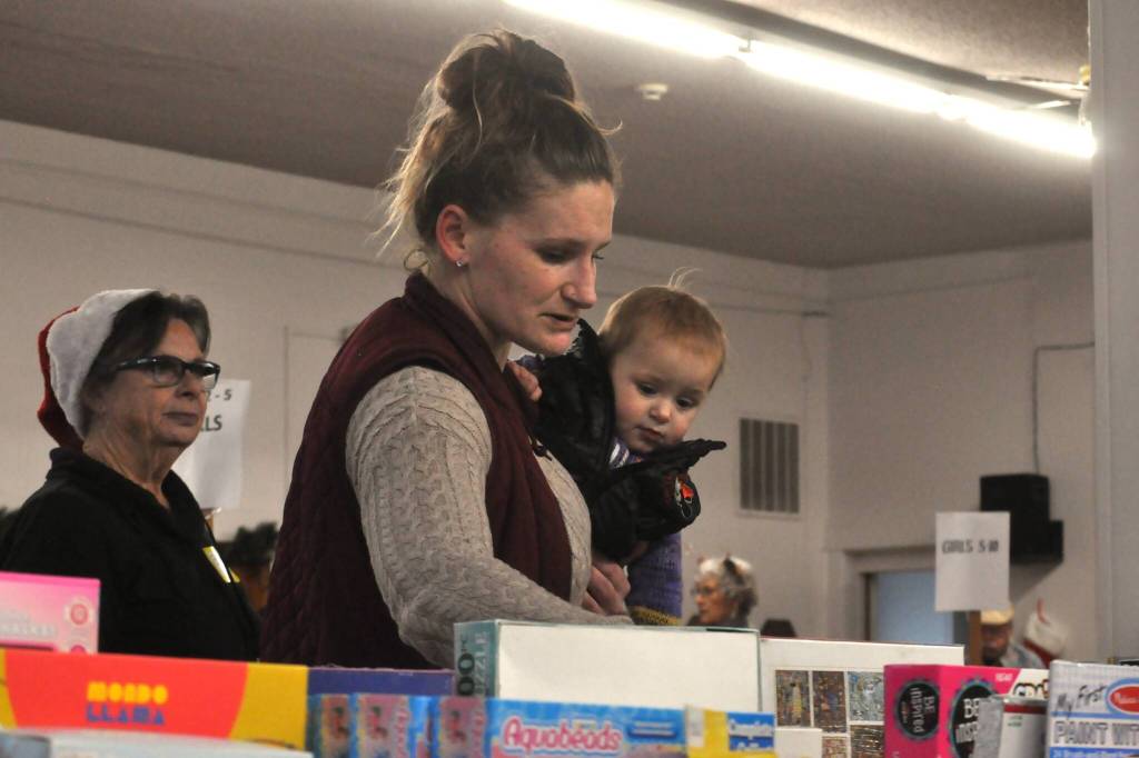 Sequim Gazette photo by Matthew Nash/
Shauna McNally with 14-month-old Baileigh looks for board games for her family as volunteer elf Bonita Jarvis, on left, helps hold her items.