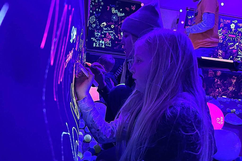Sequim Gazette photo by Matthew Nash/ Sisters Clara and Paige Cerfogli of Sequim enjoy the Glow Zone at the Sequim Sunshine Festival where they drew pictures on paper with bright markers underneath black lights.