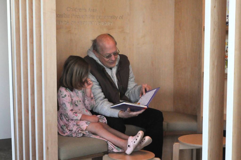 John Bays reads Grumpkin to his four-year-old daughter Linden in a seating area inside the renovated Sequim Library shortly after reopening on Saturday. Were big readers and we missed the library, Bays said.