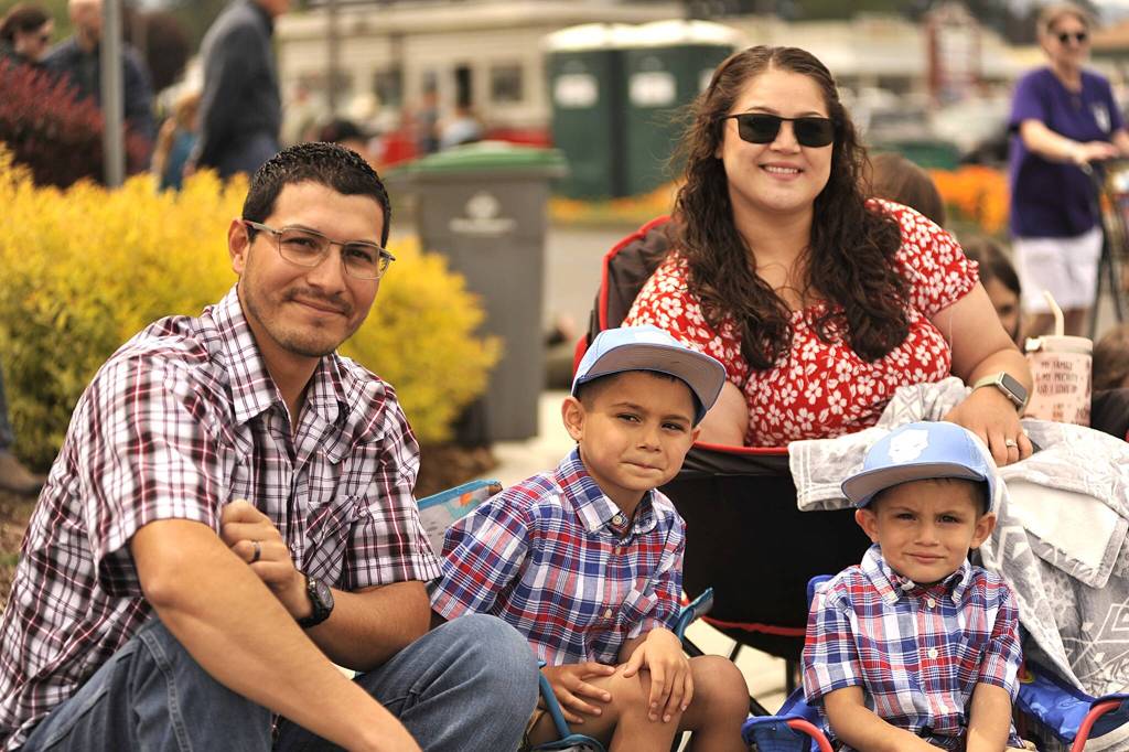 Sequim Gazette photo by Matthew Nash
Family members, from left, Samuel, Benji, Bianca and Arlo Aceves Espinoza sit and watch the Grand Parade near its end in front of Sound Community Bank. Bianca said they come every year to watch.