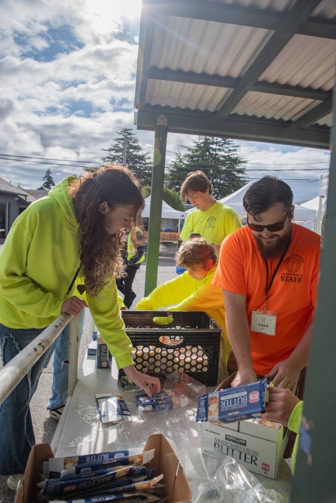 Photo by Emily Matthiessen 
Sequim Food Bank Transportation and Saturday Distribution Coordinator Cole Tierney, in orange shirt, works with students in preparation for three hours of food distribution on a recent Saturday. In the background, in a yellow shirt, is Brayden Baritelle, 15, who was 13 when he became the youngest volunteer to receive the food banks Junior Volunteer of the Year Award. He was recently among the first to receive a new Youth Award as part of the annual Clallam County Service Awards.
