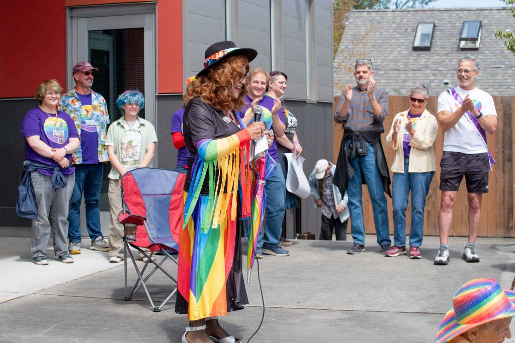 Sequim Gazette photo by Emily Matthiessen/
Sequim Pride founder Michael Lowe speaks to the gathering on Saturday at the Sequim Farmers and Artisans Market dressed as Rhoda Gravel. Behind, more of the speakers and organizers stand. From left to right, Toby Hendrickson, Glenn Kenyon, Zee French, Adam Bernbaum, Jenny Bingham Blen, Mark Ozias, Lisa Boulware and Curt Queyrouze.