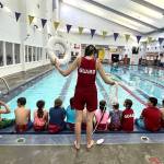 Savannah Minker, lifeguard and lead swim lesson instructor at the Y, demonstrates water rescue techniques to youth participating in Mini Lifeguard Camp.