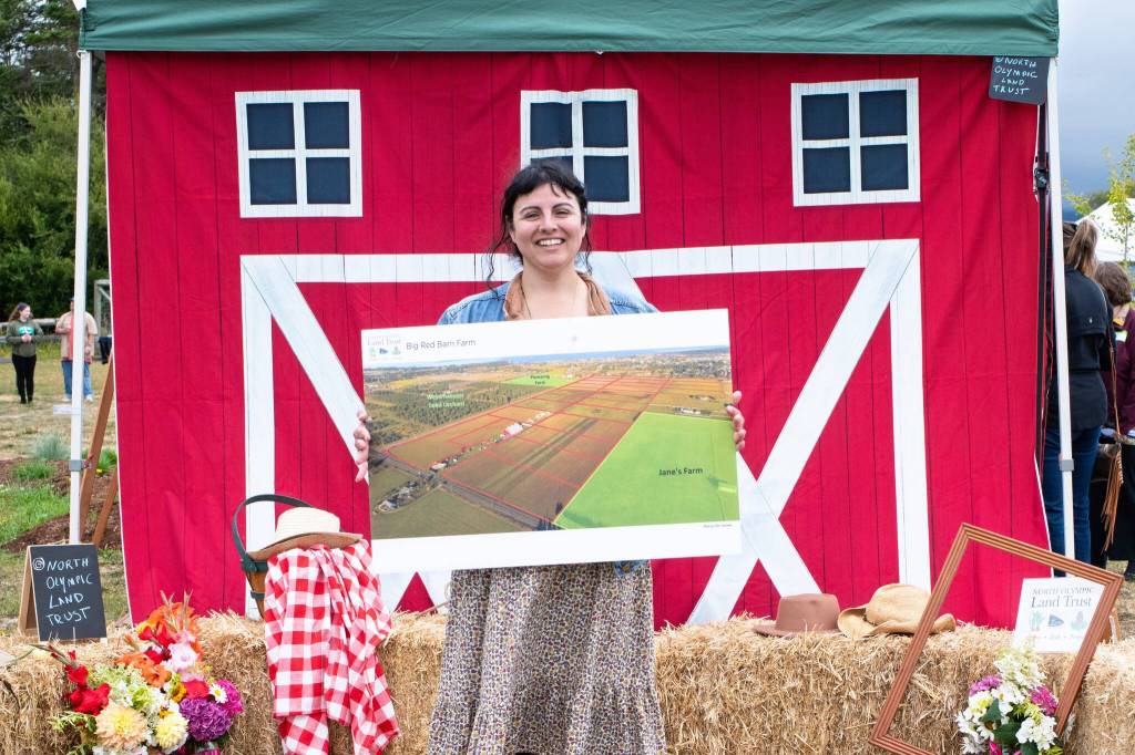 Sequim Gazette photo by Monica Berkseth/ Ayisha Jaffer, the North Olympic Land Trusts community relations director, holds a poster of the Big Red Barn Farms property that the trust looks to preserve as farmland forever.