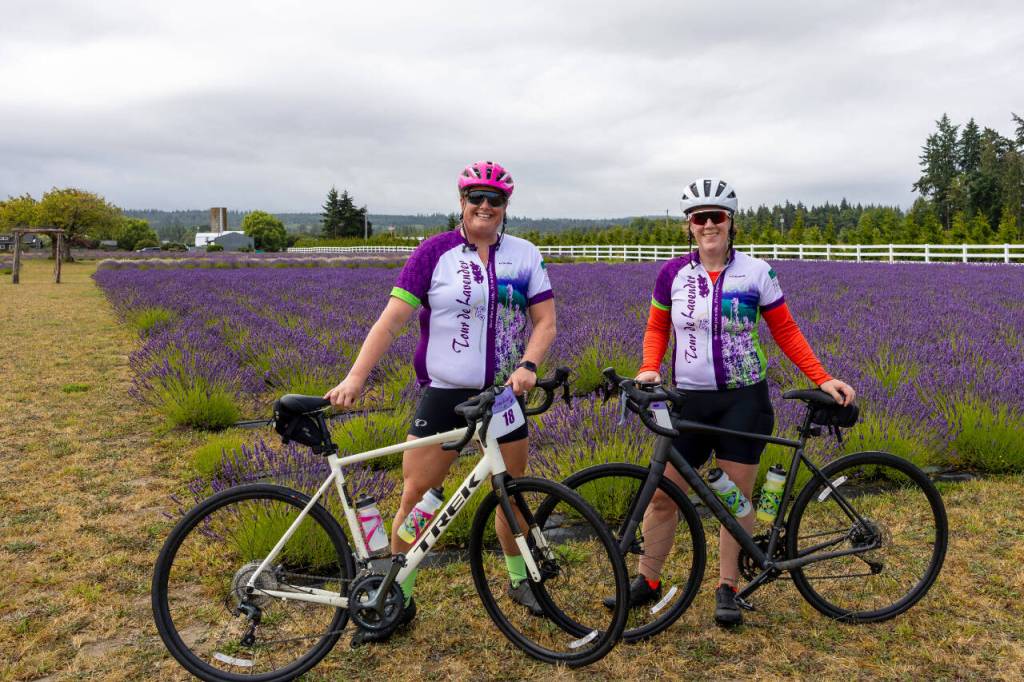 Zoe Anderson, left, and her wife, Ruth Anderson, both of Olympia, pose with their bicycles at Olympic Bluffs Cidery & Lavender Farm late Saturday morning, Aug. 1, as they participated for the first time in the annual Tour de Lavender bicycle tour of area lavender farms. The pair said they learned of the event through social media and that the lavender fields, views of the sea and organization of the ride would bring them back. Proceeds support the Peninsula Trails Coalitions work on the Olympic Discovery Trail.