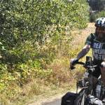 Seren McClurken, a trail ambassador with the Peninsula Trails Coalition, watches as US Army veteran Patrick Smith of Florida rides his bike along the Olympic Discovery Trail on Monday, Aug. 3. He was set to ride for 74 days from Washington, D.C. to La Push, and stopped in Sequim on day 73.