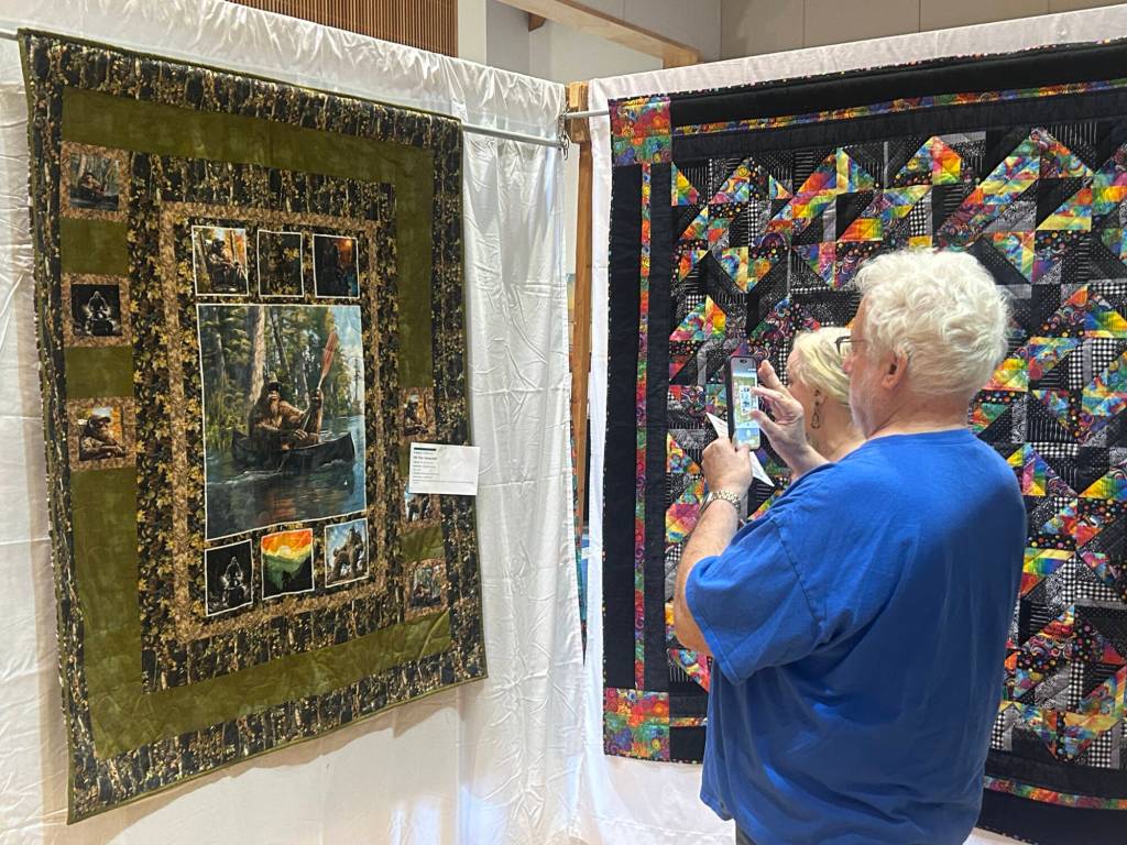 Sequim Gazette photo by Matthew Nash/ Greg Cherney with Kathy Pomeroy of California take a photo of the Sasquatch quilt by Rae Jean Dickinson. The couple said theyre particularly fond of Sasquatches.